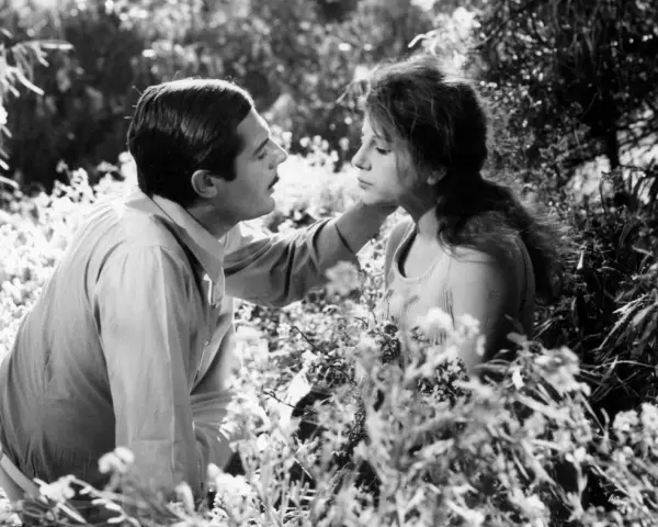 Un uomo e una donna in un campo fiorito, un'immagine che evoca il significato del sorpasso, un momento di intimità e cambiamento.