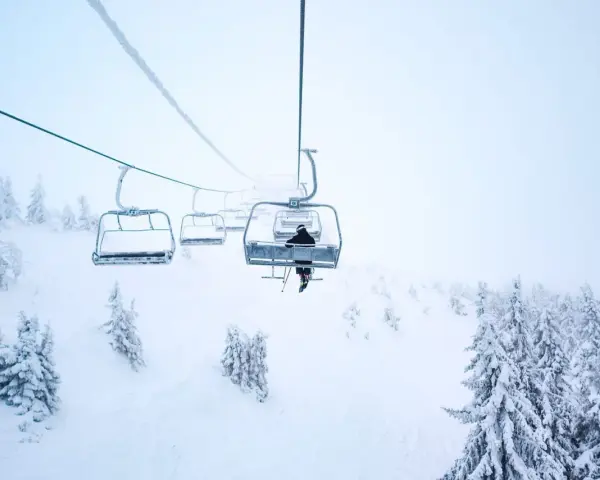 En skidåkare åker linbana uppför ett snötäckt berg i Norge, omgiven av frostiga träd.