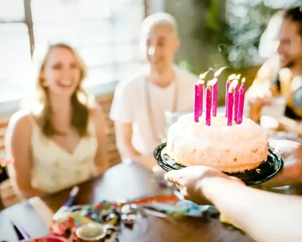 Radosne życzenia na 20 urodziny! Tort z płonącymi świeczkami, uśmiechnięci przyjaciele w tle.