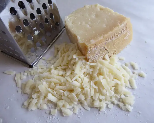 Tarty kawałek parmezanu i świeżo starty ser obok tarki. Dowiedz się, jak przechowywać parmezan, by zachował świeżość.