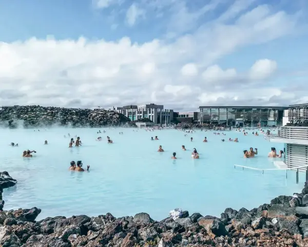 Ludzie kąpią się w turkusowej wodzie geotermalnej Blue Lagoon, otoczonej wulkanicznymi skałami i nowoczesnymi budynkami.