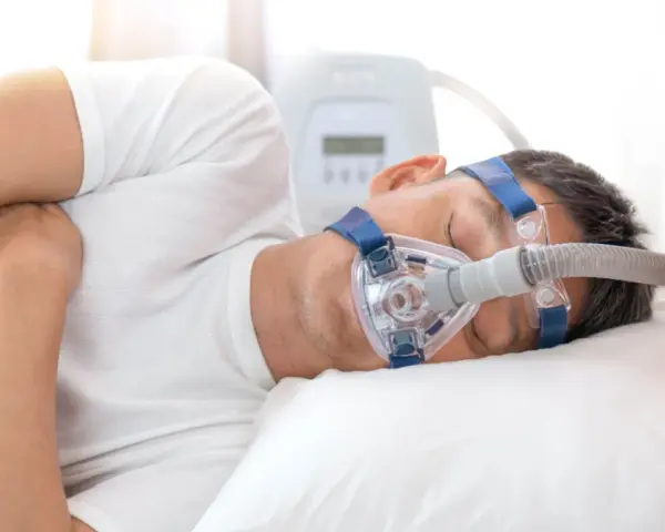 Mężczyzna śpi z maską CPAP, która pomaga mu oddychać podczas bezdechu sennego.