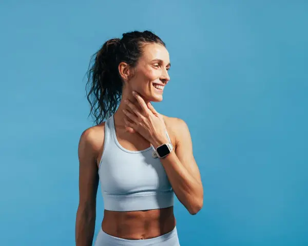 Donna sorridente con orologio sportivo, tocca il collo. Nonostante la sensazione di correre con la febbre, il suo sguardo è positivo.
