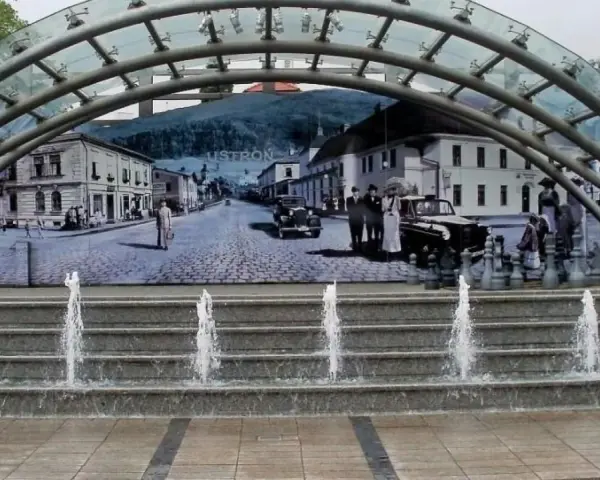 Ustroń rynek: fontanna i mural przedstawiający historyczne miasto z ludźmi w strojach z epoki i zabytkowymi samochodami.
