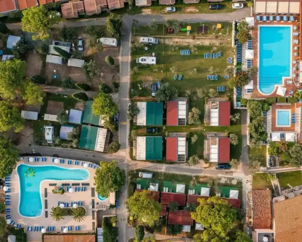 Widok z lotu ptaka na camping Toscolano: domki, baseny, przyczepy kempingowe i zielone tereny.