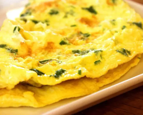 Złożony omlet z zielonymi ziołami na białym talerzu.