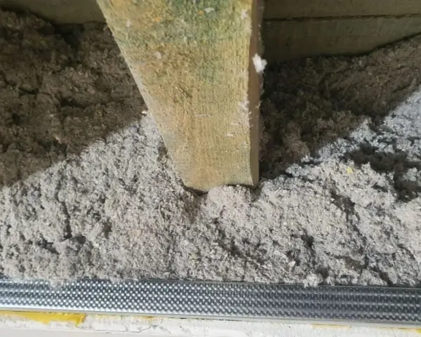 Luźna wełna celulozowa, widoczne nierówności i potencjalne wady izolacji pod drewnianą belką stropową.