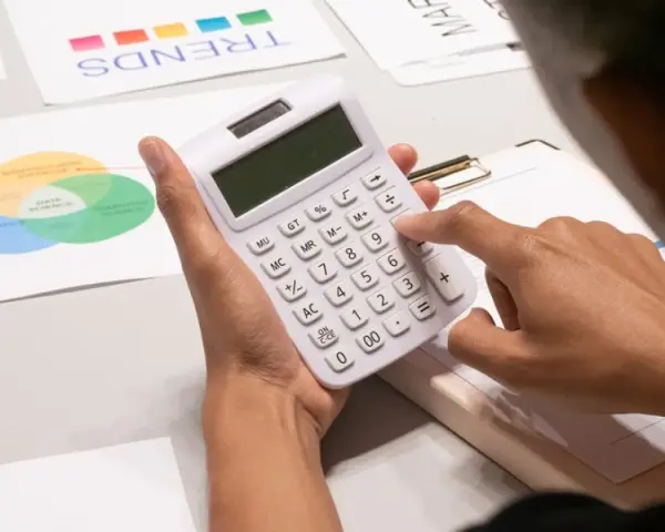 Persona calculando con calculadora blanca, rodeada de gráficos de tendencias y diagramas de Venn, analizando datos para gestionar masas patrimoniales.