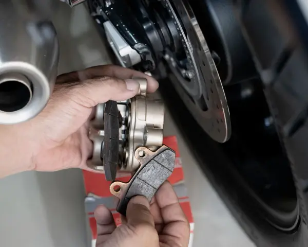 Mani che sostituiscono le pastiglie dei freni anteriori di una moto. Si valuta la durata pastiglie freni anteriori osservando l'usura.