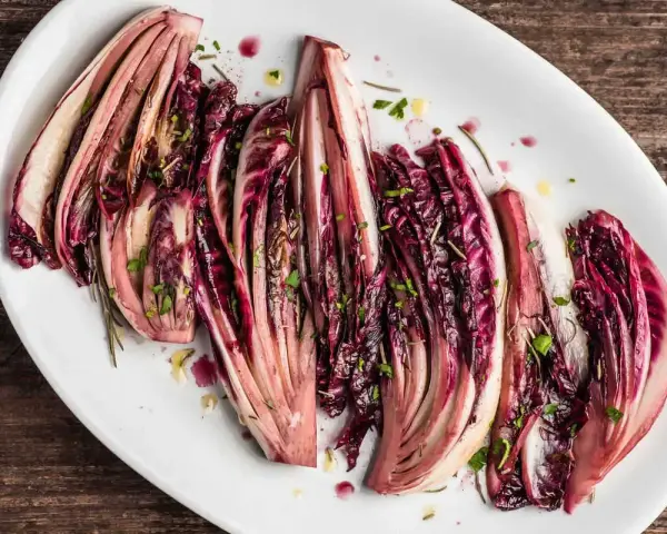 Radicchio al forno, tagliato a spicchi e condito con erbe aromatiche, servito su un piatto bianco.