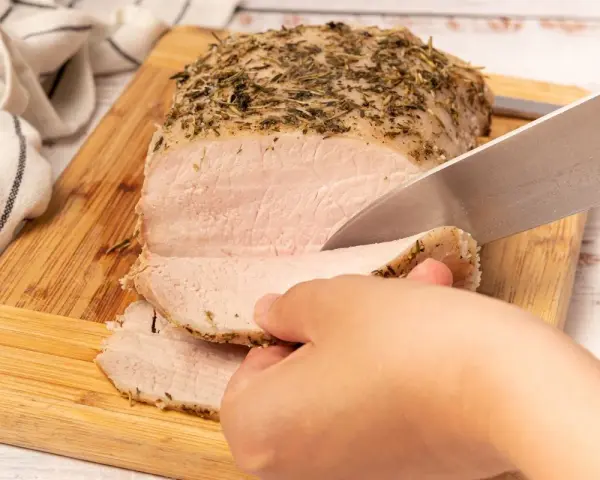 Un jugoso lomo a la sal, cubierto de hierbas, se corta en rodajas tiernas sobre una tabla de madera.