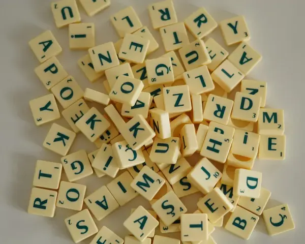 Fichas de letras de un juego de mesa, como las del Scrabble, dispersas. Cada ficha tiene una letra y un número. Un ejemplo visual de la diferencia entre lengua e idioma.