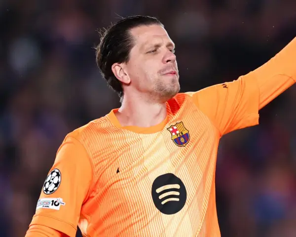 Wojciech Szczęsny w pomarańczowej koszulce bramkarskiej FC Barcelony, z podniesioną ręką, gotowy do obrony.