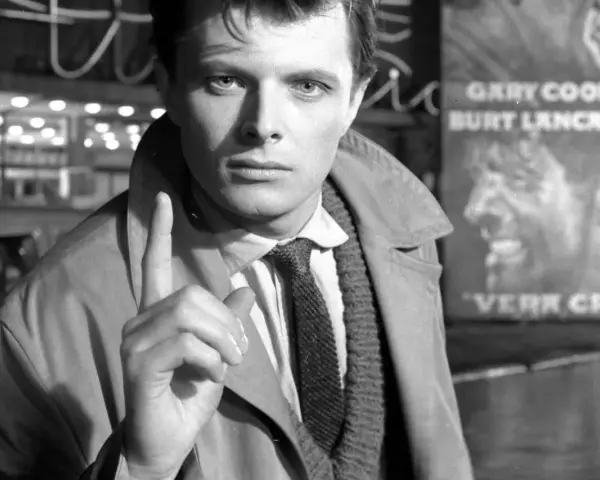 Młody Andrzej Maj, z palcem uniesionym w geście ostrzeżenia, stoi przed plakatem filmu "Werr Cruz" z Garym Cooperem.