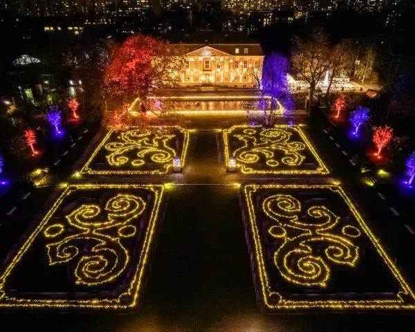 Magische Lichtershow im Tierpark Berlin: Verzauberte Gärten mit leuchtenden Mustern und farbig beleuchteten Bäumen vor einem prachtvollen Gebäude.