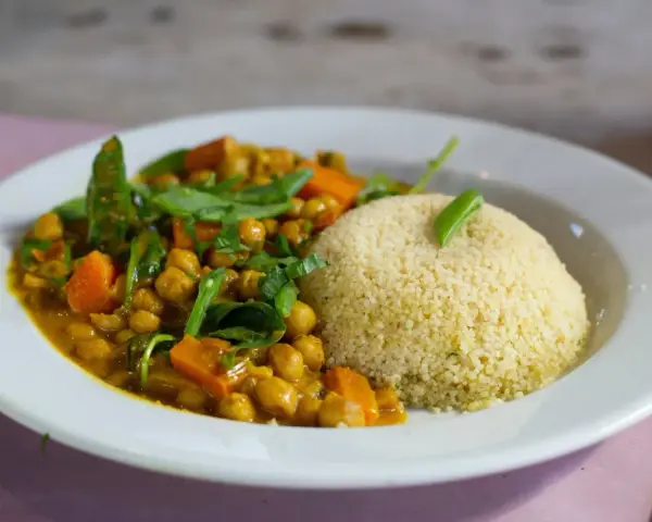 Un plato de cuscus con verduras, garbanzos y zanahoria en una salsa dorada, decorado con hojas verdes.