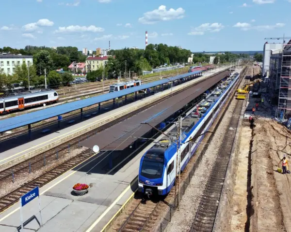 Widok z góry na dworzec kolejowy w Kielcach z pociągami na torach i placem budowy.