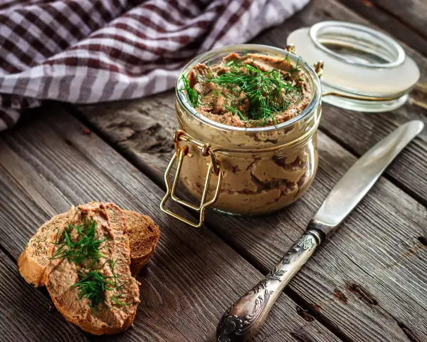 Un tarro de rillettes, paté de cerdo desmenuzado, con eneldo fresco, servido sobre pan tostado.