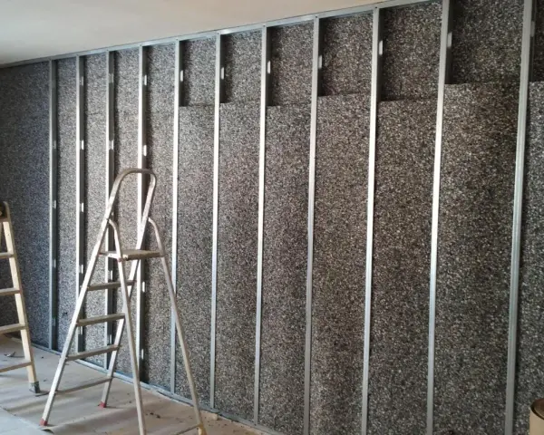 Instalación de material para insonorizar pared. Escaleras apoyadas contra la estructura metálica y el panel aislante.