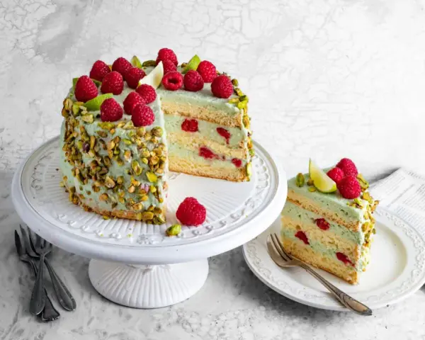 Wyjątkowy tort pistacjowy z malinami i limonką, ozdobiony chrupiącymi pistacjami. Idealny na każdą okazję.