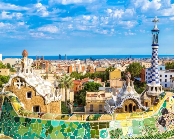 Kolorowe mozaiki i fantazyjne budowle Parku Güell, dzieło Antonio Gaudiego, na tle błękitnego nieba i Barcelony.