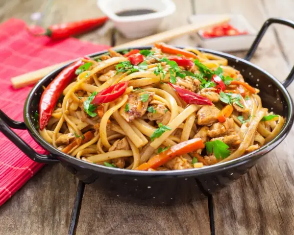 Pyszny makaron chain main z kurczakiem, papryką i chili, posypany natką pietruszki, w czarnej woku.