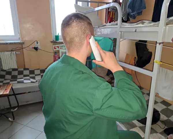 Mężczyzna w zielonym uniformie rozmawia przez telefon. Czeka na odpowiedni moment, po jakim czasie więzień może dzwonić do rodziny.