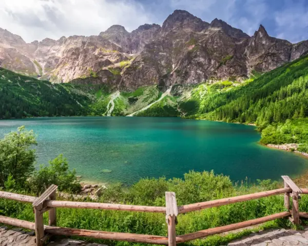 Turkusowe jezioro otoczone zielonymi zboczami gór i lasem, przypominające beskidzkie Morskie Oko.