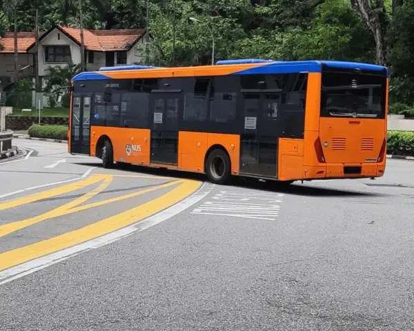 Pomarańczowo-niebieski autobus miejski na zakręcie drogi z żółtymi pasami.