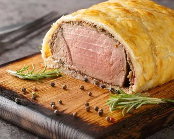 Wołowina Wellington na desce z rozmarynem i pieprzem.