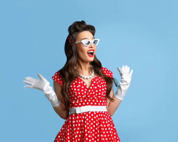 Kobieta w czerwonej sukience w grochy i białych rękawiczkach, z białymi okularami, prezentuje stylizacje pin up girl.