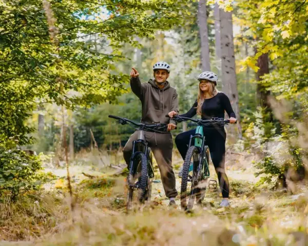 Para rowerzystów w kaskach na leśnej ścieżce. Mężczyzna wskazuje drogę, odkrywając piękną trasę w Szklarskiej Porębie.