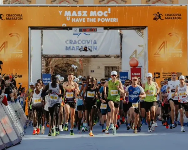 Zawodnicy przekraczają linię startu Maratonu Cracovia. Tłum kibiców z telefonami dokumentuje to wydarzenie.