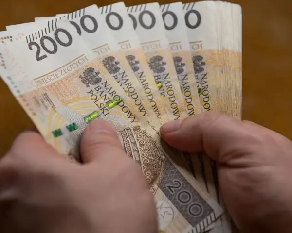 Dłonie trzymają stos banknotów po 200 zł. Czy to wystarczy, by poznać, ile wynosi najniższa krajowa netto?