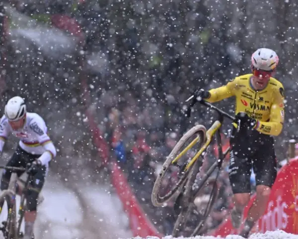 Cyclists battle snowy conditions. Wout van Aert, in yellow, appears to be recovering from a crash, while another rider in white pushes on.