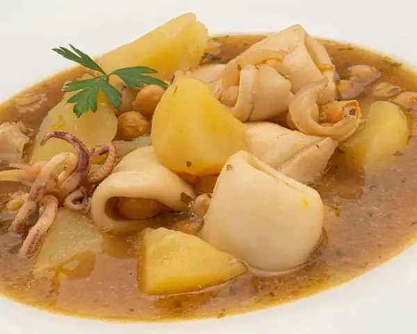 Guiso de garbanzos con trozos de calamar, patatas y perejil en un plato blanco.