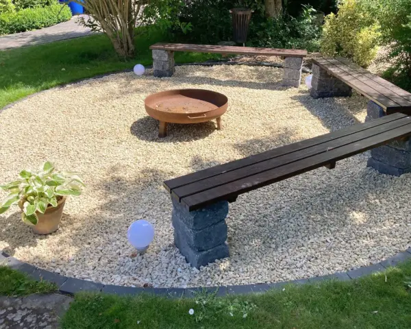 Gemütliche Sitzecke im Garten mit Kiesboden, Feuerstelle und Holzbänken. Perfekt für laue Sommerabende.