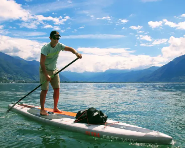 Mann auf SUP-Board mit Paddel, genießt die Geschwindigkeit auf dem See vor einer Bergkulisse.