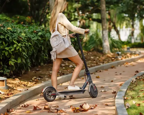 Ragazza su monopattino elettrico in un parco autunnale. Ricorda l'obbligo casco monopattino per la tua sicurezza.