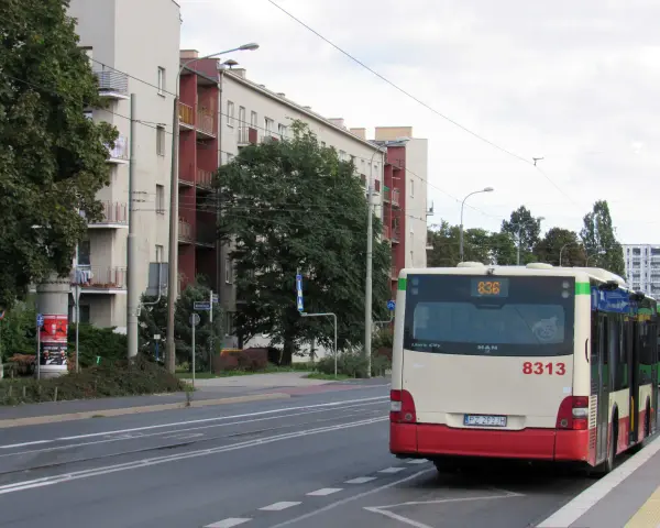 Autobus 8313 z numerem linii 836 czeka na przystanku. W tle budynki mieszkalne i drzewa.