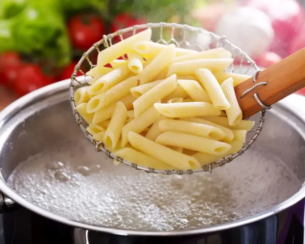 Penne w cedzaku nad garnkiem z wrzącą wodą. Prosty sposób, jak ugotować makaron do ulubionego sosu.