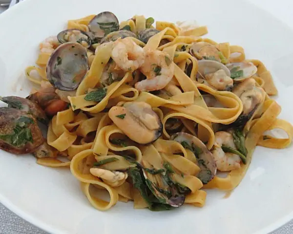 Un piatto invitante di tagliatella di mare con gamberi, cozze e vongole, condita con erbe fresche.