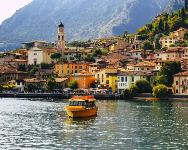 Un giallo battello solca il lago, dirigendosi verso il pittoresco borgo di Limone sul Garda, con le sue case colorate aggrappate alla montagna.