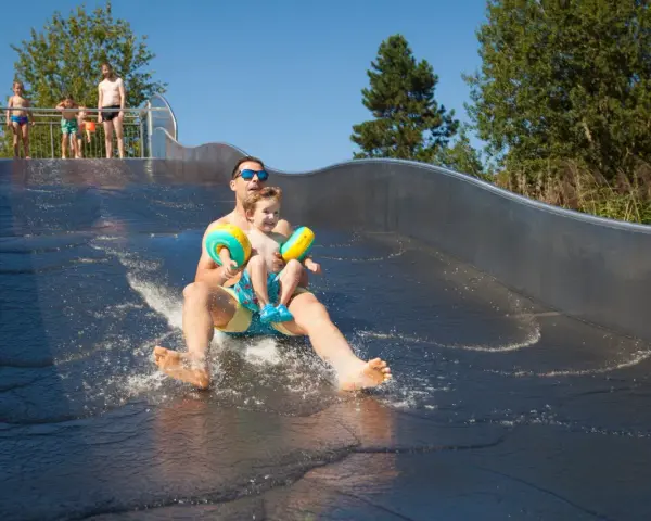 Vater und Sohn rutschen lachend die Wasserrutsche im Bostalsee Strandbad hinunter.
