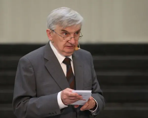 Starszy mężczyzna w garniturze, który prowadzi jeden z dziesięciu, trzyma kartkę.