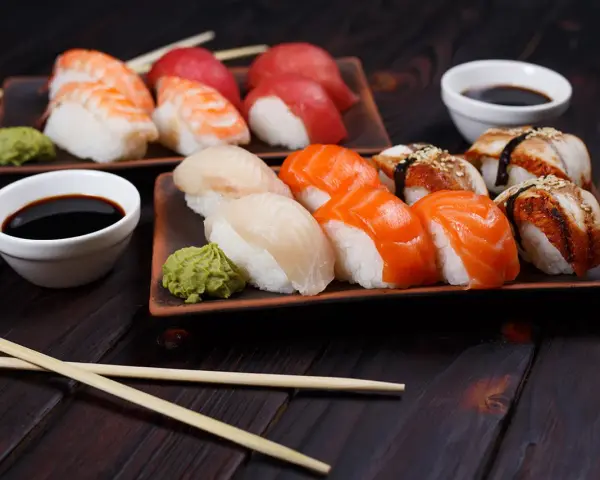 Różnorodne rodzaje sushi: nigiri z krewetką, łososiem, białym rybą i węgorzem, podane z wasabi i sosem sojowym.