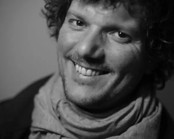 Uśmiechnięty Filip Ćwik w szarym szaliku, z kręconymi włosami i zarostem.