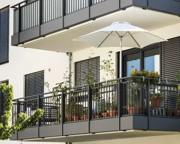 Nowoczesny balkon po remoncie, z białym parasolem i doniczkami pełnymi zieleni.