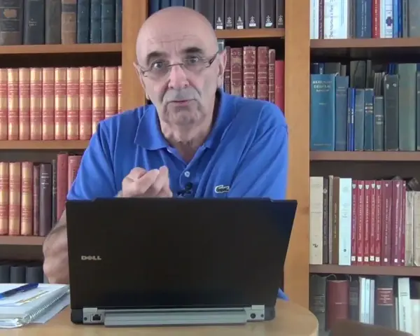Un homme parle devant un ordinateur portable, entouré de rayonnages remplis de livres anciens, rappelant les archives départementales 85.