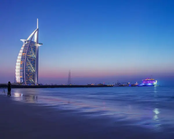 Zachód słońca nad Zatoką Perską. Widok na hotel Burj Al Arab i oświetloną łódź. Ceny w Dubaju mogą być wysokie, ale widoki są bezcenne.